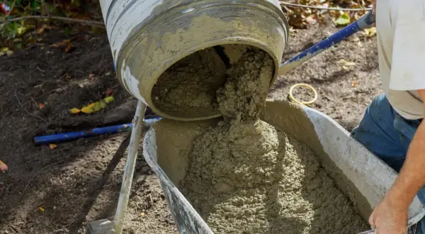 Betoniarka wylewa świeży beton do taczki, przygotowując materiał budowlany.